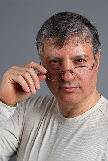 Studioaufnahme mit Sergio. Person steht vor einer Neuralen Wandund schau über seine Brille hinweg.  