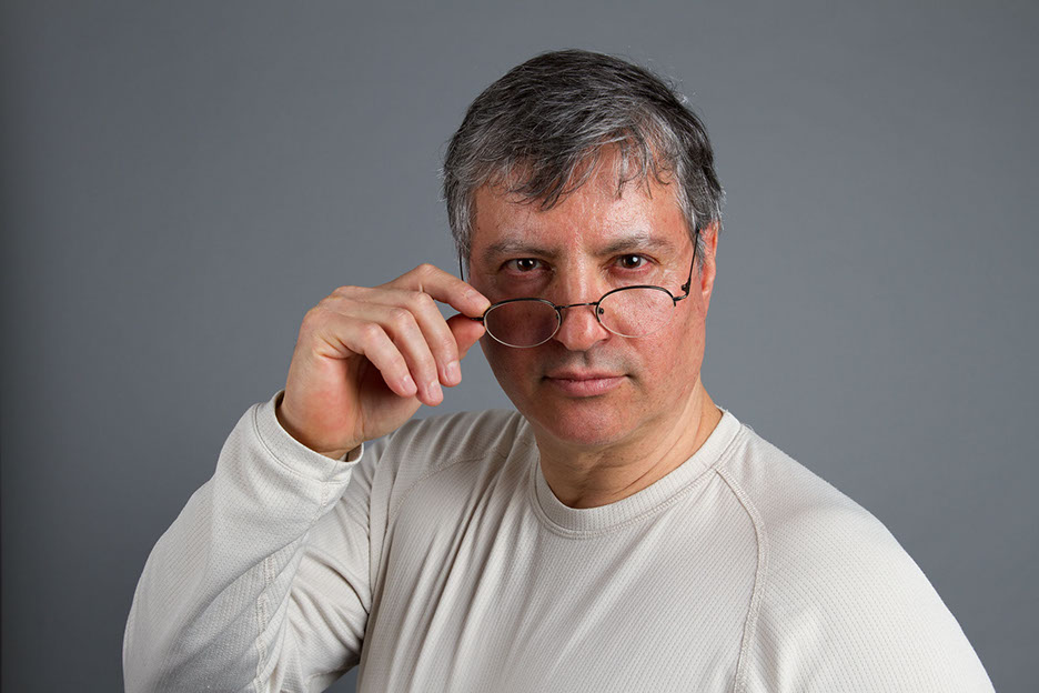 Studioaufnahme mit Sergio. Person steht vor einer Neuralen Wandund schau über seine Brille hinweg.  